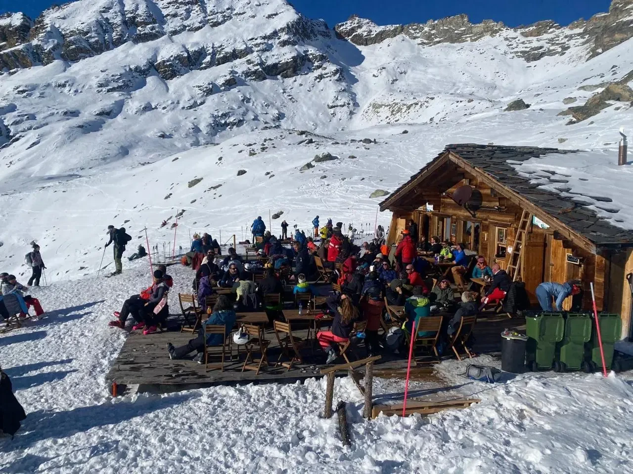 La terrasse de La Chotte remplie de skieurs au soleil, cabane en bois et cirque enneigé — Arolla, 2 166 m